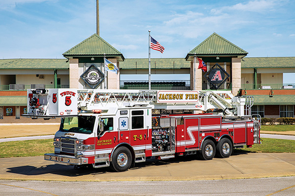 White over red colored aerial fire truck parked in front of city building in summer