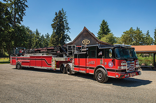 Officers side of tiller fire truck parked in front of building on sunny day