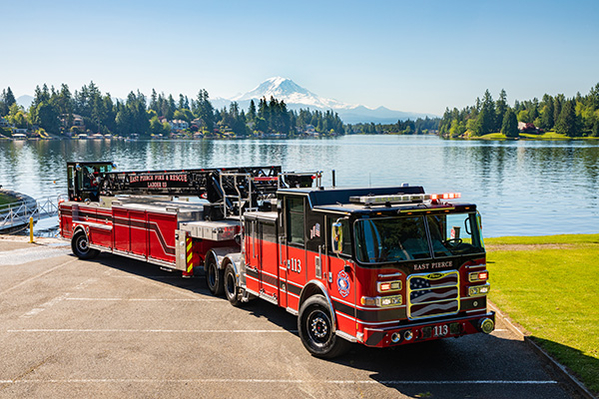 Tiller ladder fire truck parked in front of water on a sunny day