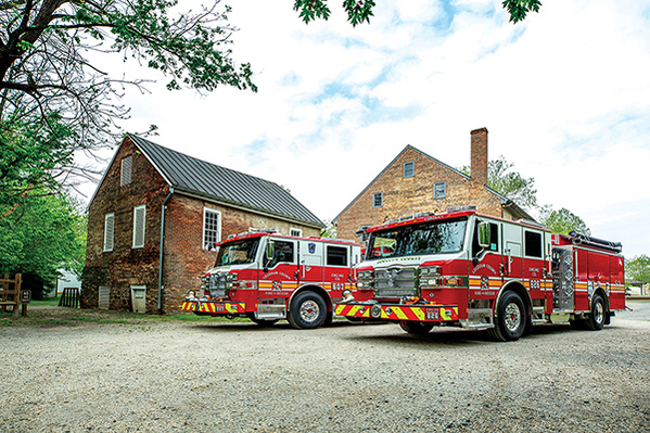 Two pumper fire trucks parked on gravel outside brick building on a mostly cloudy day