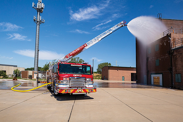 Aerial ladder fire truck spraying water from the ladder tip onto brick building