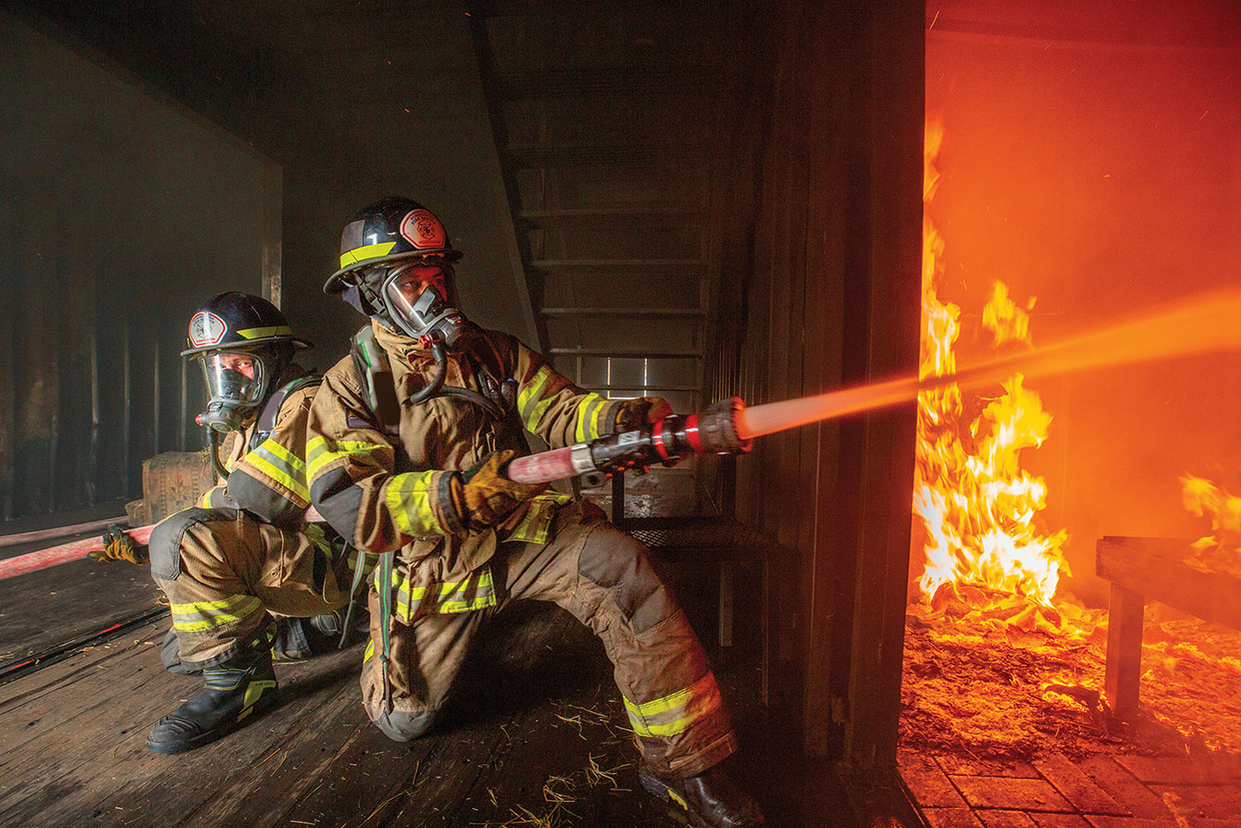 Two firefighters spraying water from nozzle on active fire
