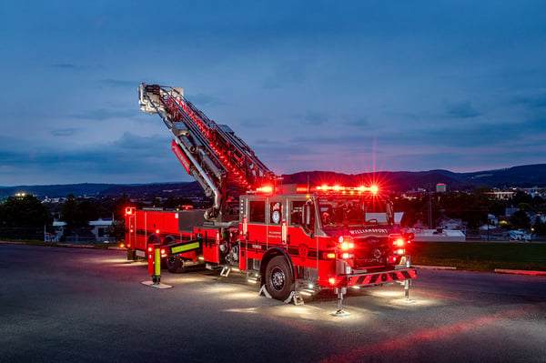 The front officers side of a Velocity 100 Ascendant Aerial Tower with the aerial ladder extended and the lights on at night.