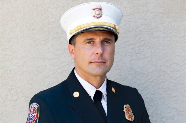 The fire chief for Folsom Fire Department in a suit and hat posed in front of a concrete wall.