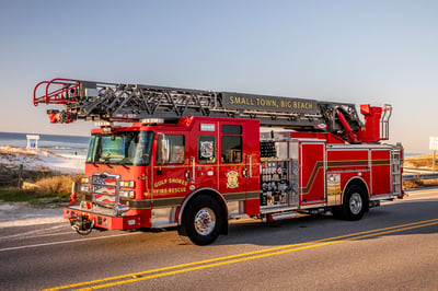 The front drivers side of an Enforcer Ascendant 107 aerial ladder driving on a road beside a beach.