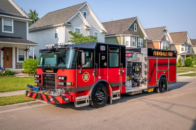 The front drivers side of a Saber Pumper fire truck driving down a residential neighborhood street.