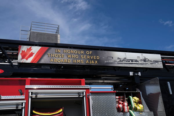 The drivers side of an Aerial Platform with a graphic on the side of the aerial ladder and hose in the crosslays.