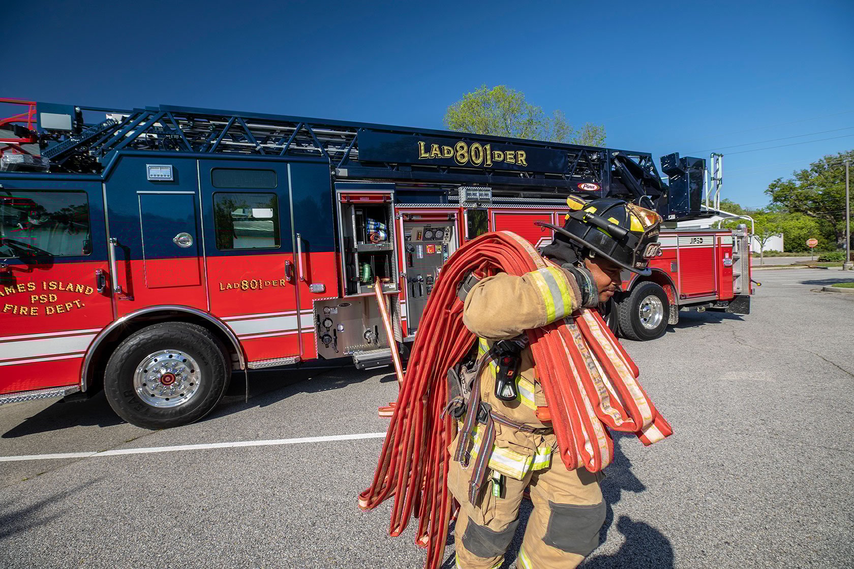 A firefighter in turnout gear pulling hose from the crosslays on an Ascendant Aerial Ladder with a PUC pump on a sunny day.