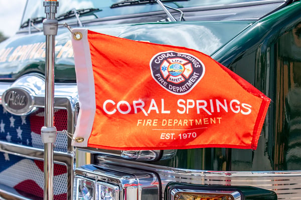 A flag with the Coral Springs Fire Department in Florida waving in the wind on the front bumper of a fire truck.
