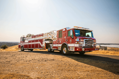 A red Pierce ladder fire truck parked in a warm dry climate.