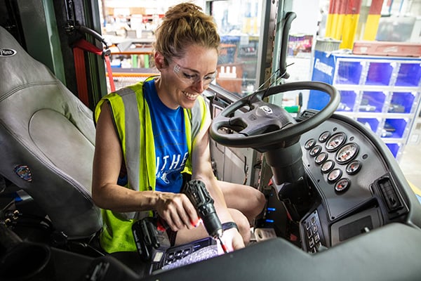 A woman sitting in the driver’s side of a Pierce Fire Truck holding a drill doing maintenance on the interior of the cab.