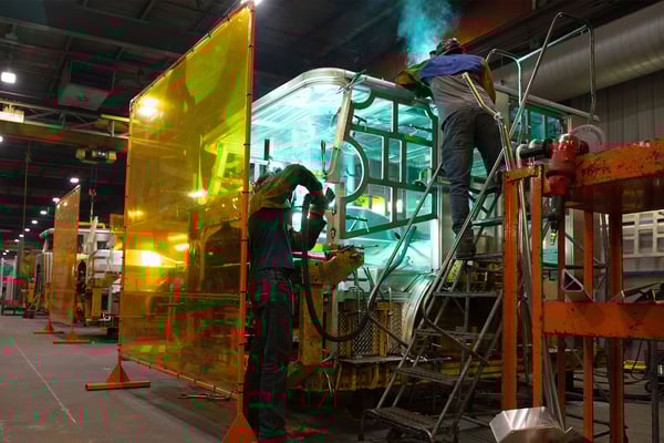 Two welders in a manufacturing building welding the cab of a fire truck together.