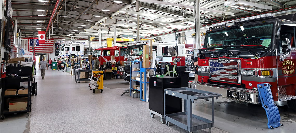 A modern fire truck manufacturing facility with fire trucks in bays with team members working on them.