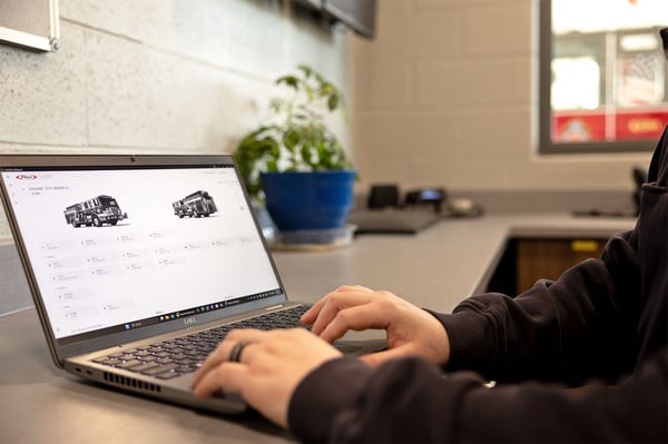 A person at a fire station working on a laptop with a screen showing data points on a fire truck. 
