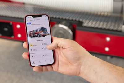 The hand of a firefighter holding a cell phone with a connected solutions application open on the phone with fire truck data on it.