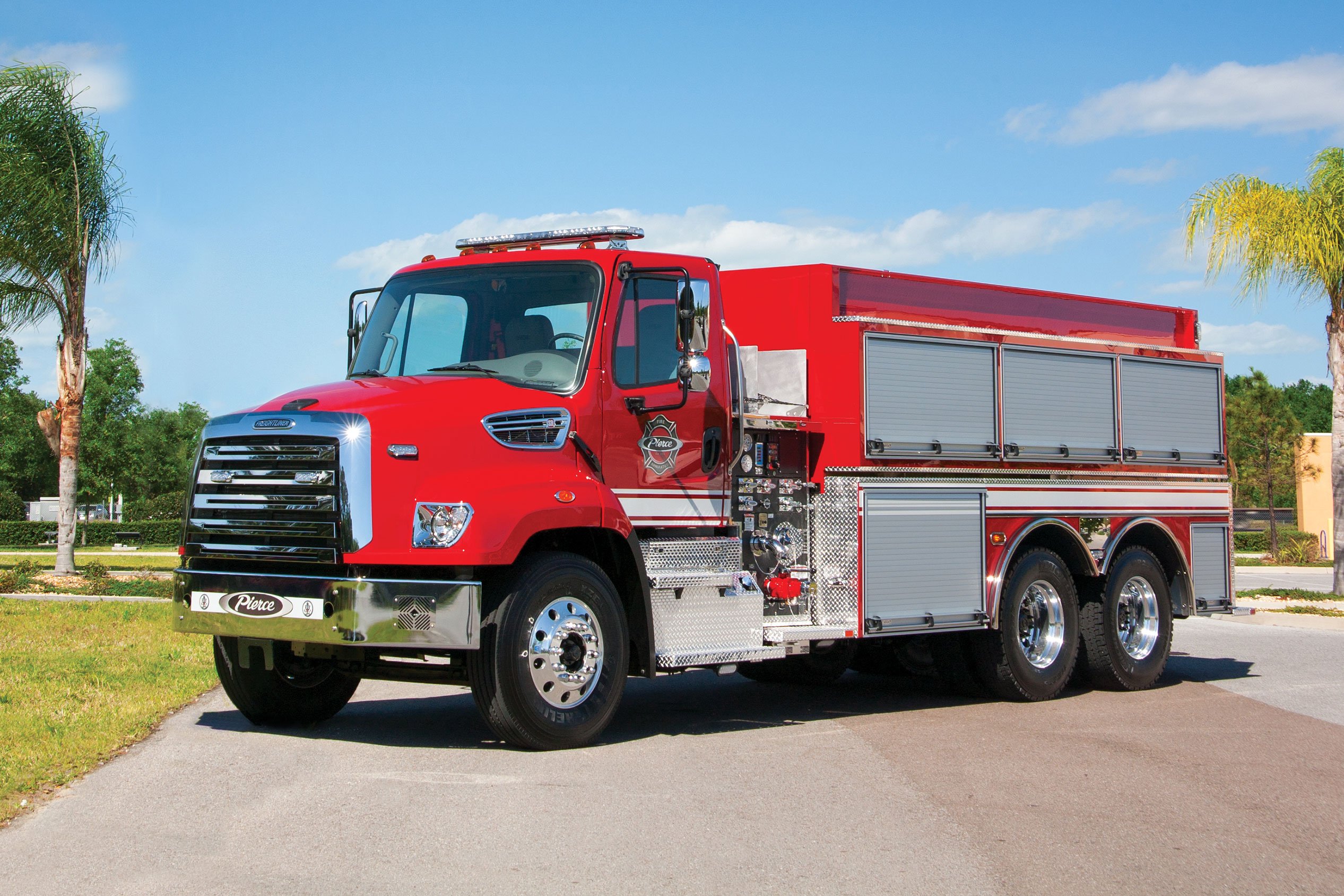 Pierce Commercial Fire Truck chassis parked outside on a sunny day near trees. 