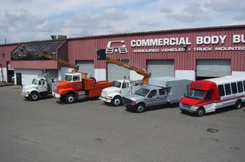 Commercial utility trucks and vehicles parked in front of the Commercial Body Builders facility.