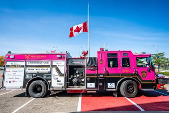 A pink fire truck is parked in a lot in front of a waving Canadian flag.