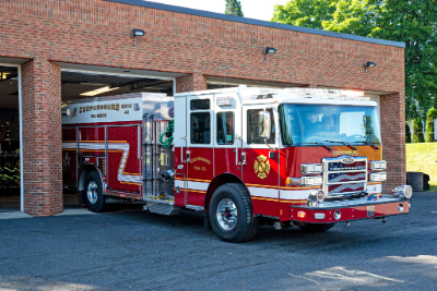 A red and white fire truck pulling out of a brick fire station.