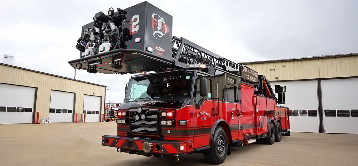 A front view of the black and red Dickinson Fire Department’s 100-foot Pierce aerial platform truck in front of two buildings with white garage doors.