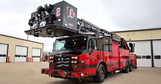A front view of the black and red Dickinson Fire Department’s 100-foot Pierce aerial platform truck in front of two buildings with white garage doors.