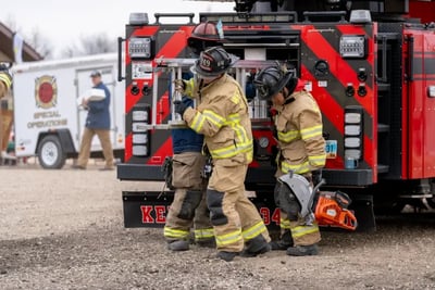 West Fargo firefighters handle rescue equipment, including a saw, by a red and black fire truck.