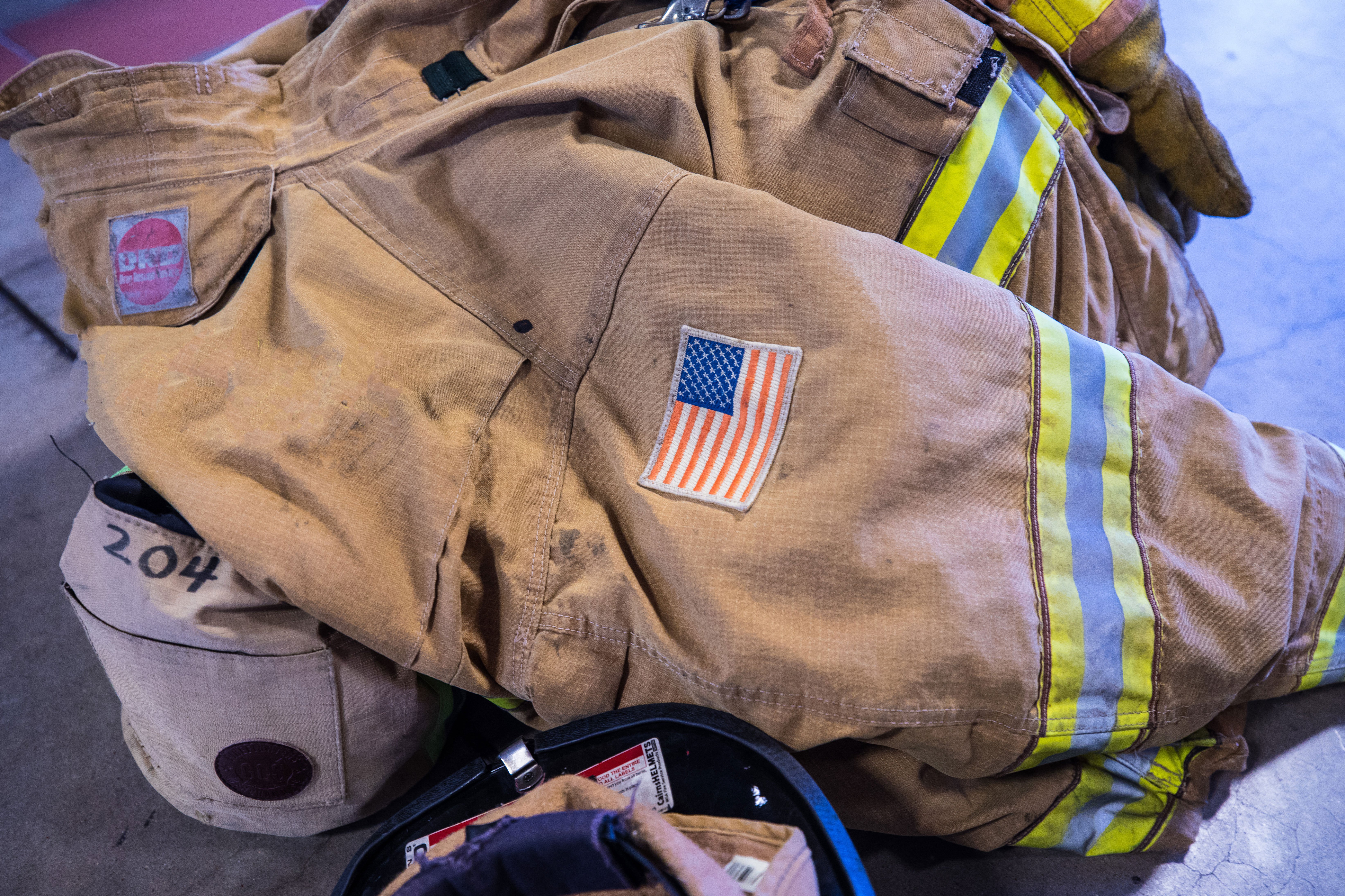 A firefighters jacket sitting on the floor next to firefighting gear.