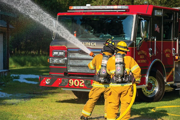 Two Firefighters pumping water through a hose next to a Pierce Fire Truck. 