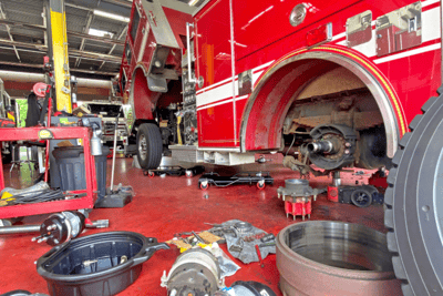 A maintenance floor scattered with equipment and materials while a fire truck wheel is being worked on.