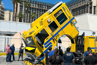 A team of people look at a lifted cab of a yellow fire truck with blue line.