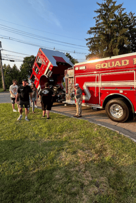 The cab of a red fire truck is tilted up while a group of people look on.