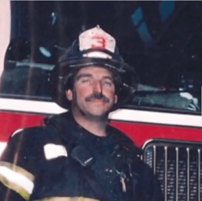 FDNY Lieutenant Kevin W. Donnelly smiling in turnout gear and helmet in front of a fire engine.