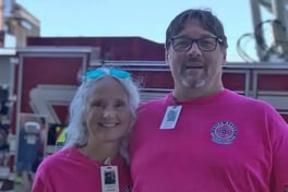 9/11 survivors John and Donna Kneeley smile in pink t-shirts in front of a fire truck.