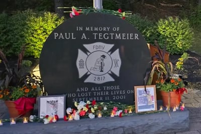 A black granite memorial stone honoring FDNY firefighter Paul A. Tegtmeier, adorned with flowers and candles.