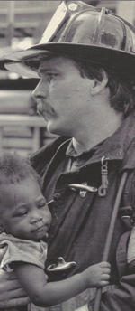 An old picture of a firefighter holding a baby.