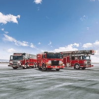 Three custom Pierce fire trucks parked outside on open terrain.