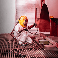 A Pierce technician in a protective suit spray-painting a red fire truck panel in a paint booth.