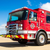 A red Pierce electric fire truck on the road with a blue sky in the background.