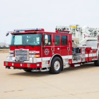 A red Pierce stock fire truck on the road with a gray sky in the background.