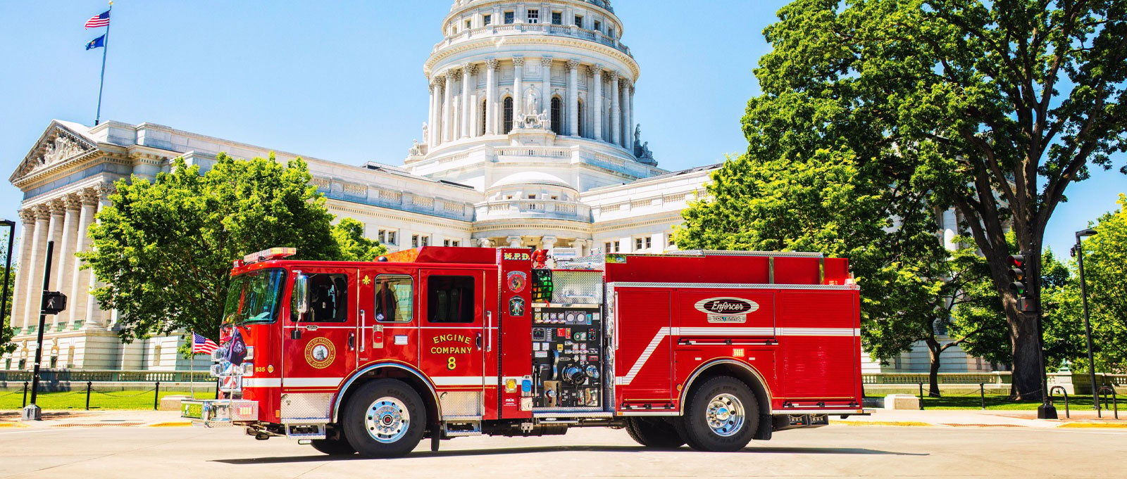 A red Pierce electric fire truck sitting on the road in front of the capital in Madison, Wisconsin.