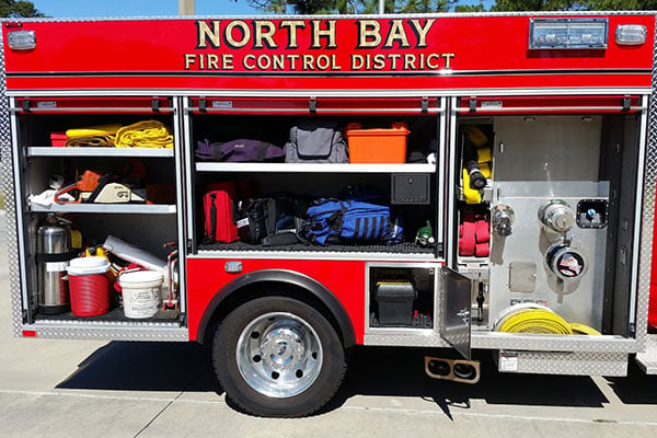 Officer’s side of a Pierce Mini Pumper Fire Truck with compartment doors open showing storage space. 