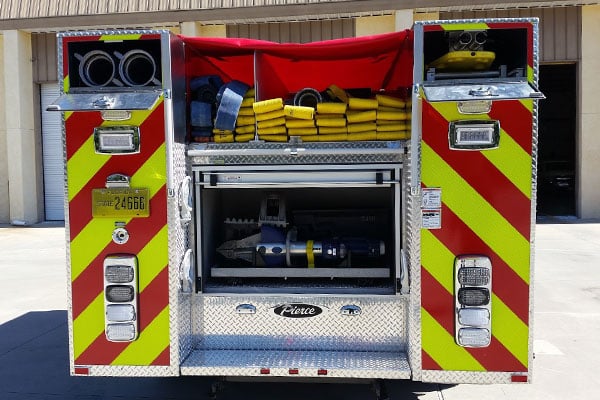 Pierce Mini Pumper Fire Truck with rear compartments open and storage space parked outside near a building. 