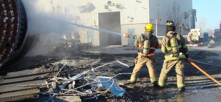 Two firefighter interns hold a fire hose and work to put out a fire outside of a building.