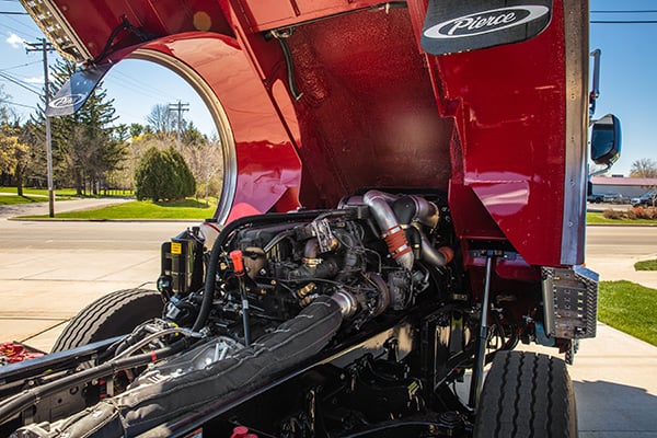 A raised Pierce Fire Truck parked outside on a sunny day showing the PACCAR MX-13 Big Block Engine underneath the cab.