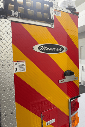 A custom fire truck plaque that reads 'Maverick' on the back of a fire truck which shows red and yellow diagonal lines.
