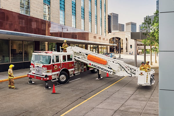 Pierce Aerial Ascendant platform fire truck parked on the street surrounded by fire fighters with fire fighters in the bucket. 