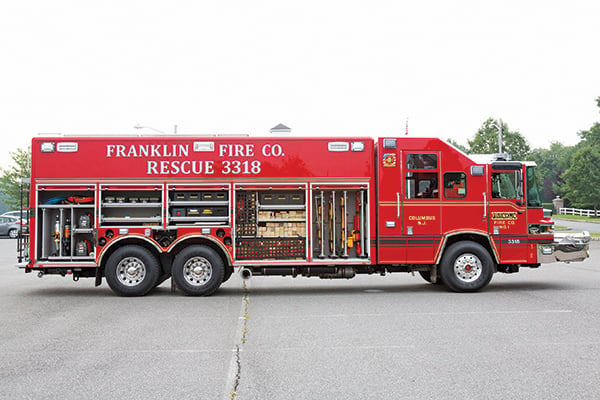 Passenger’s side of a Pierce Combination Heavy-Duty Rescue Fire Truck parked outside in a parking lot with side compartments open showing storage space. 