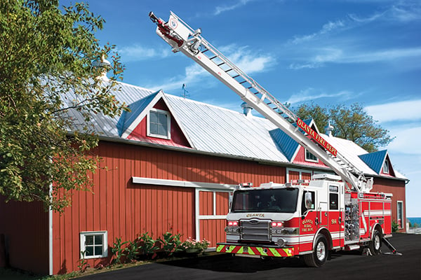 Pierce Heavy-Duty Sky-Boom Aerial Tower Fire Truck parked outside in front of fire station with ladder ascending into the sky. 