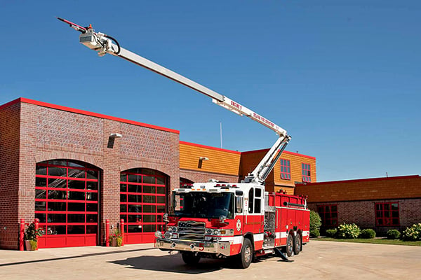 Pierce Fire Truck parked outside on a sunny day in front of a Fire Station with the High-Reach Snozzle extended in the air in front of the apparatus. 