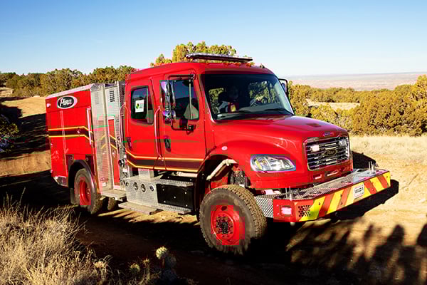 Officer’s side of a Pierce BX™ Wildland Fire Truck parked outside near trees on a sunny day.